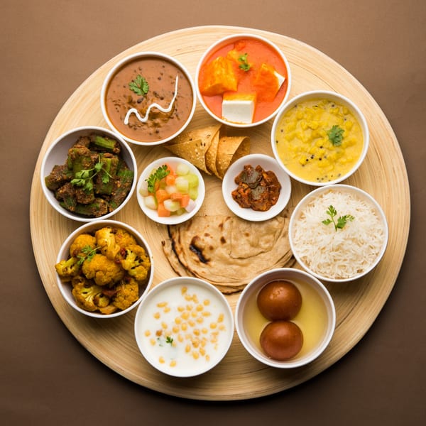 A Janaki Indian Cuisine thali with various curries, rice, bread, and desserts on a wooden platter.