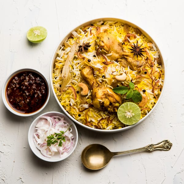 Chicken Biryani with lime, sauce, and onion raita, served on a white textured surface.